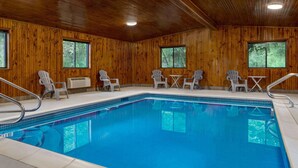 Una habitación con paneles de madera, una piscina, sillas y mesas blancas.
