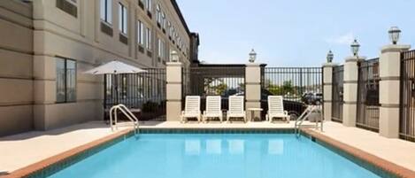 A swimming pool with a brick border, surrounded by a building with multiple windows and a gated entrance.