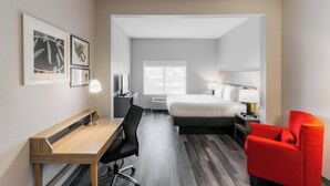 A hotel room with a bed, desk, chair, and a bright red armchair. - Townhome Inn And Suites (Cordova)