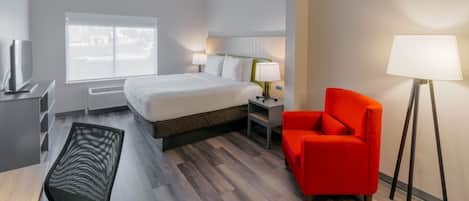 Quarto de hotel moderno com uma cama grande, luminárias de cabeceira, uma poltrona vermelha e uma escrivaninha com televisão de tela plana.