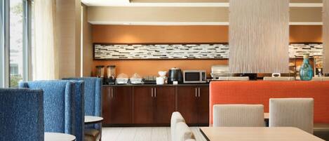 A hotel lobby with seating areas, a counter with a coffee machine, and a decorative wall.