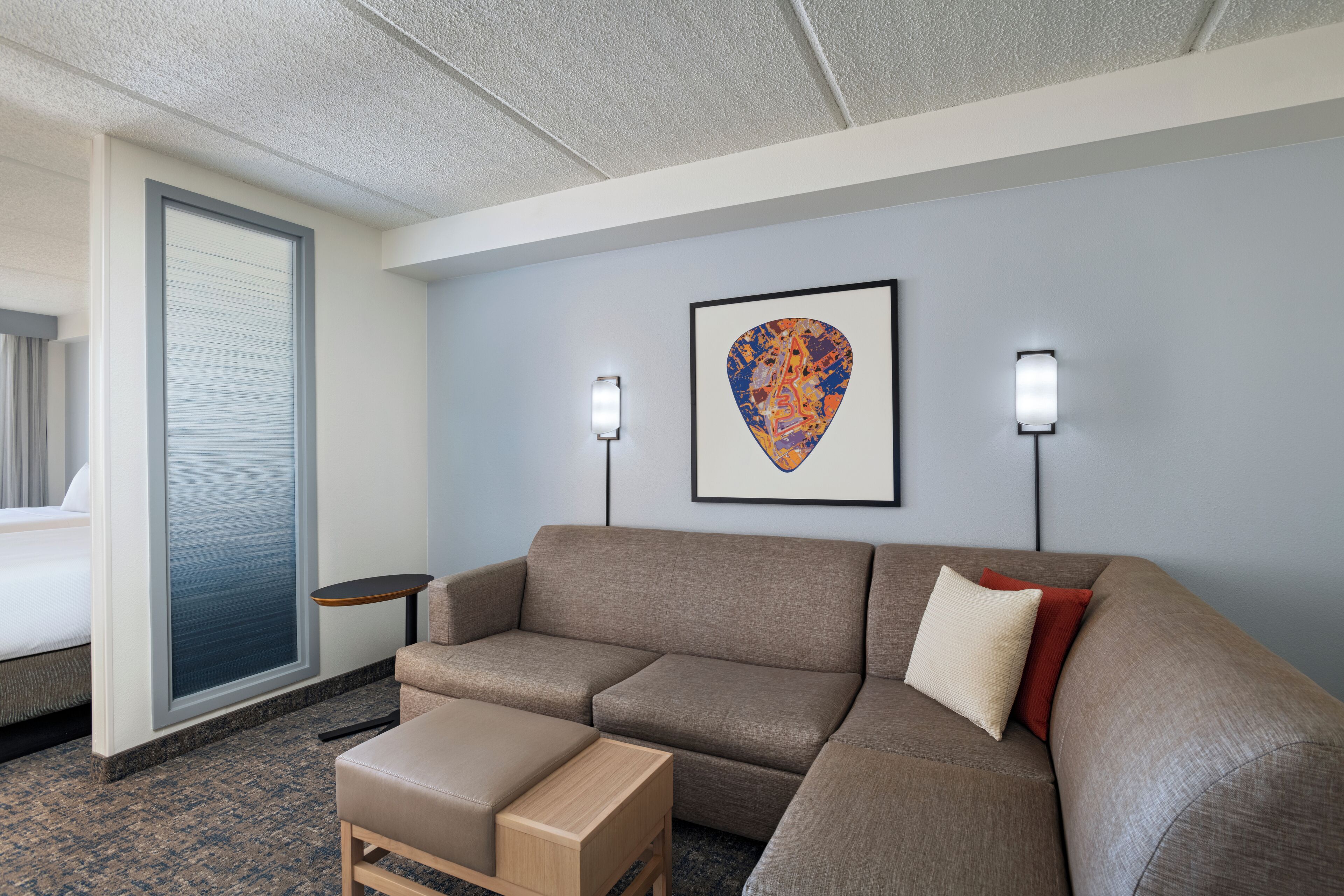 A modern hotel room with a sectional sofa, a small wooden table, and a framed artwork on the wall.