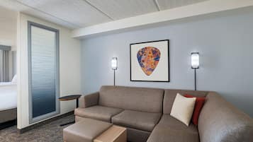 A modern hotel room with a sectional sofa, a small wooden table, and a framed artwork on the wall.