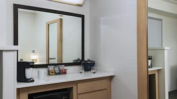 A hotel bathroom with a large mirror, a coffee maker, a tea maker, and a sink.