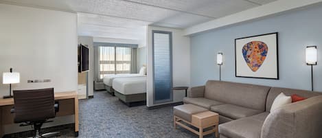 Habitación de hotel con cama, escritorio, silla, sofá, una mesita y un cuadro en la pared.