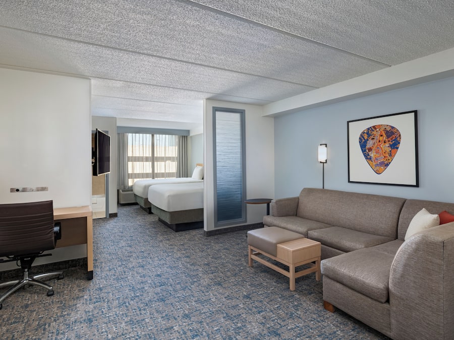Habitación de hotel con cama, escritorio, silla, sofá, una mesita y un cuadro en la pared.