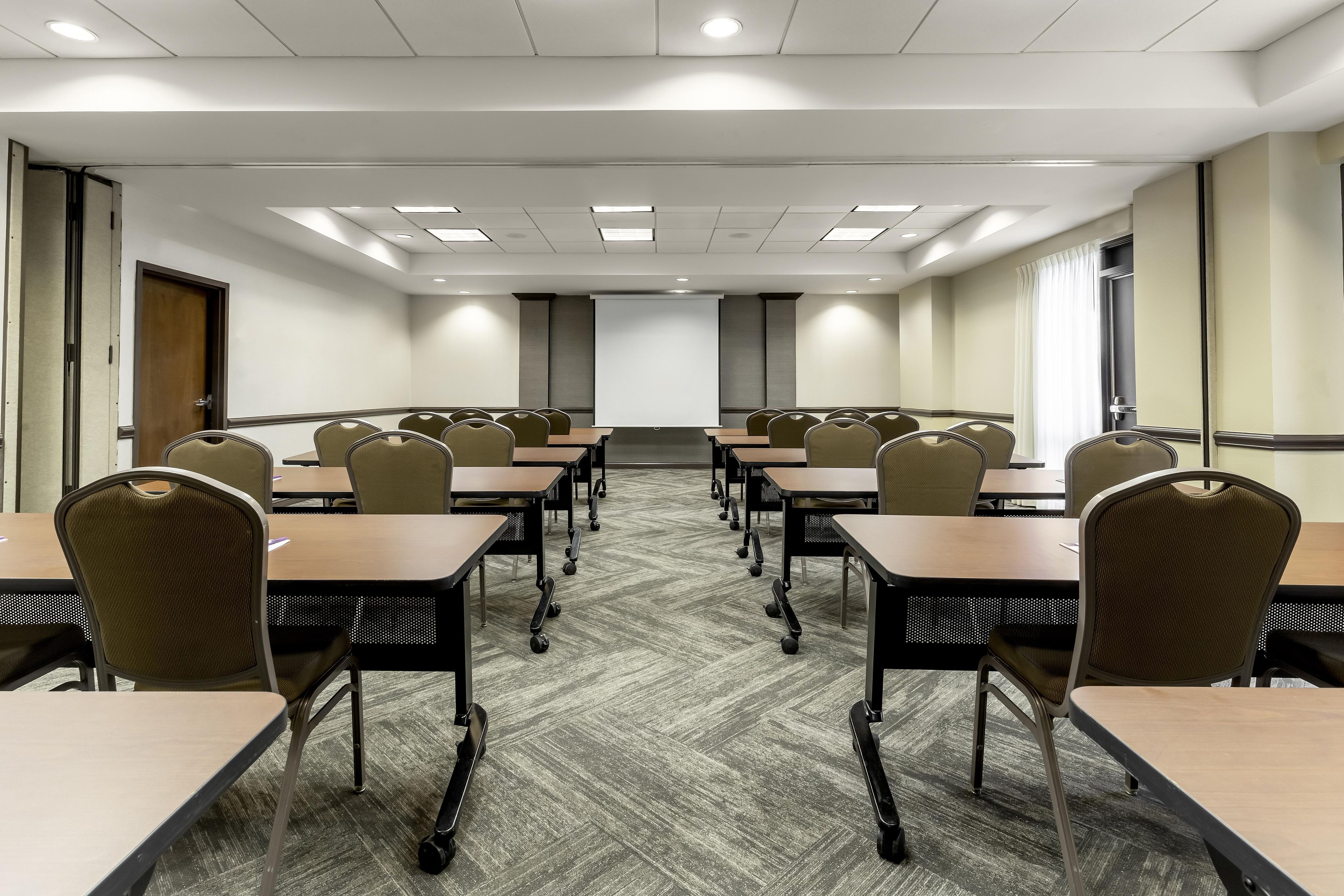 A conference room with tables and chairs, a projector screen, and a carpeted floor.