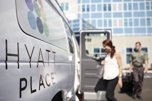 A white van with "HYATT PLACE" written on it, parked in front of a building with a blue and white facade.