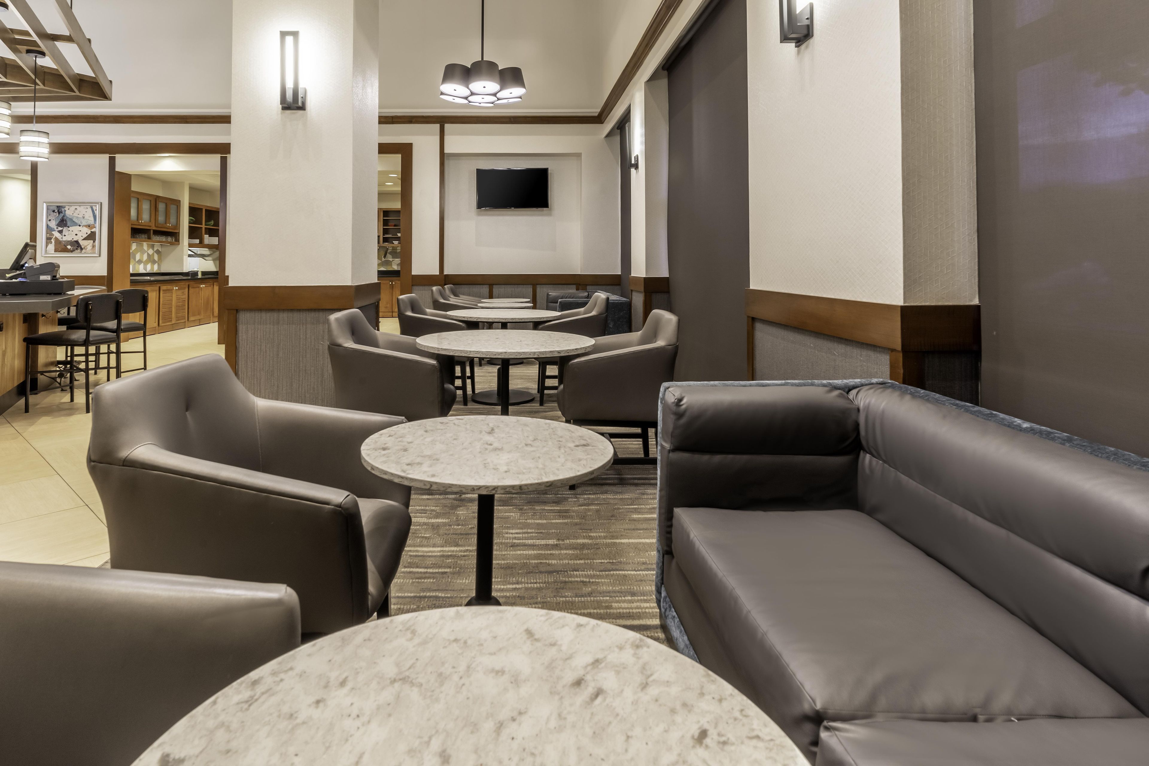 A hotel lobby with seating arrangements, a flat-screen TV mounted on the wall, and a reception desk.