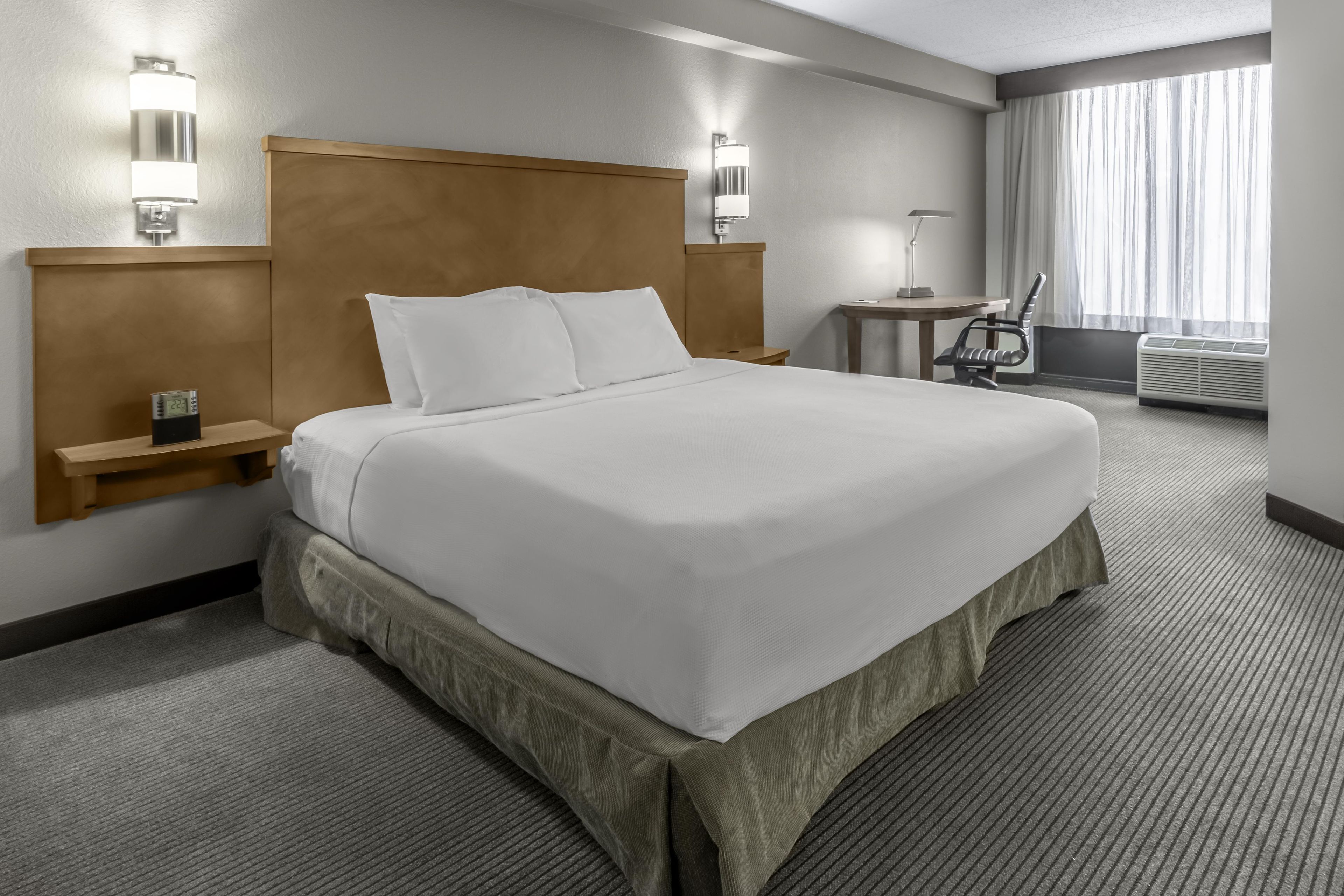 A hotel room with a large bed, bedside lamps, a desk, and a chair.