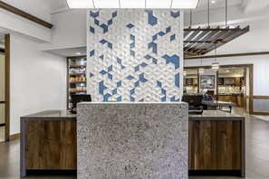 A reception desk with a marble top, a patterned wall, and a modern kitchen area in the background. - Hyatt Place Charlotte Airport / Billy Graham Parkway (Charlotte)