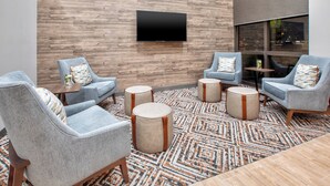 Un área de descanso moderna con un televisor de pantalla plana montado en una pared de madera, sillones azul claro con detalles marrones y una alfombra estampada.
