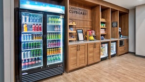 Un quiosco de bebidas con una variedad de refrescos y aperitivos, mueble de madera y un letrero que dice "CANDLEWOOD CUPBOARD".
