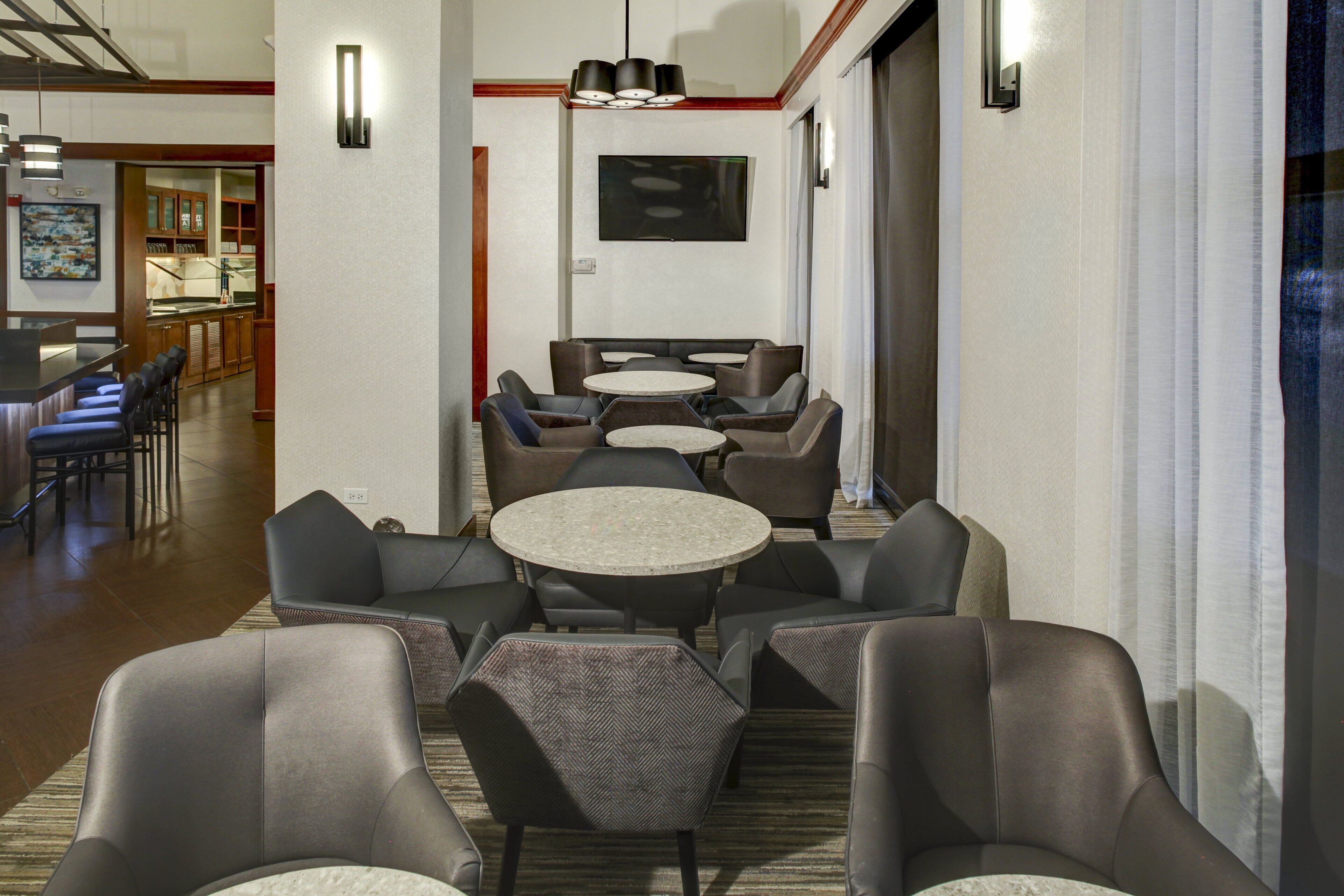 A hotel lobby with round tables and chairs, a bar area, and a television mounted on the wall.