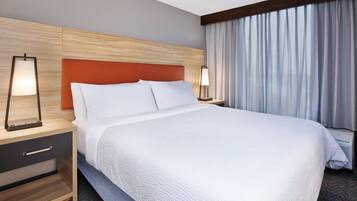A hotel room with a large bed, a wooden headboard, a nightstand with a lamp, and a window with curtains.