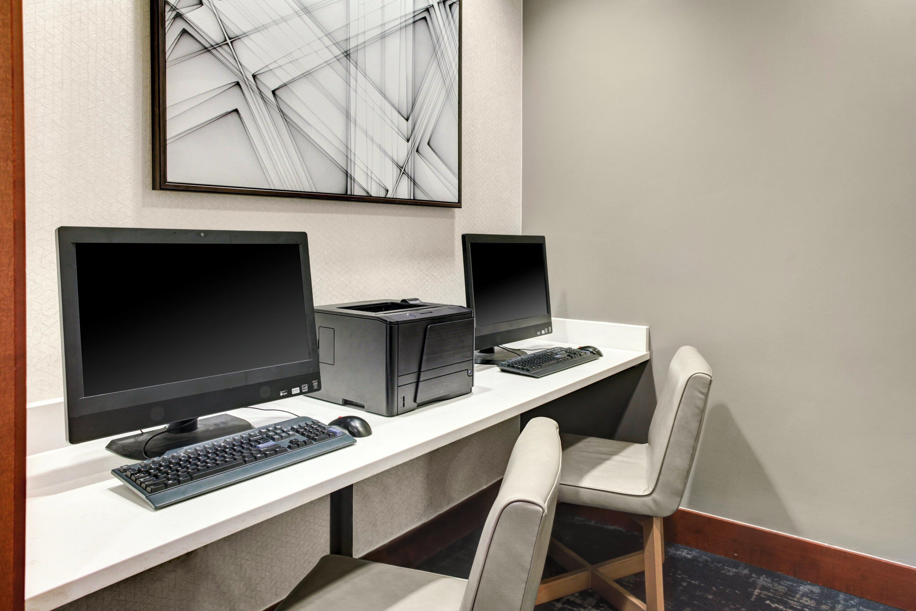 A workspace with two monitors, a printer, and a keyboard on a white desk.