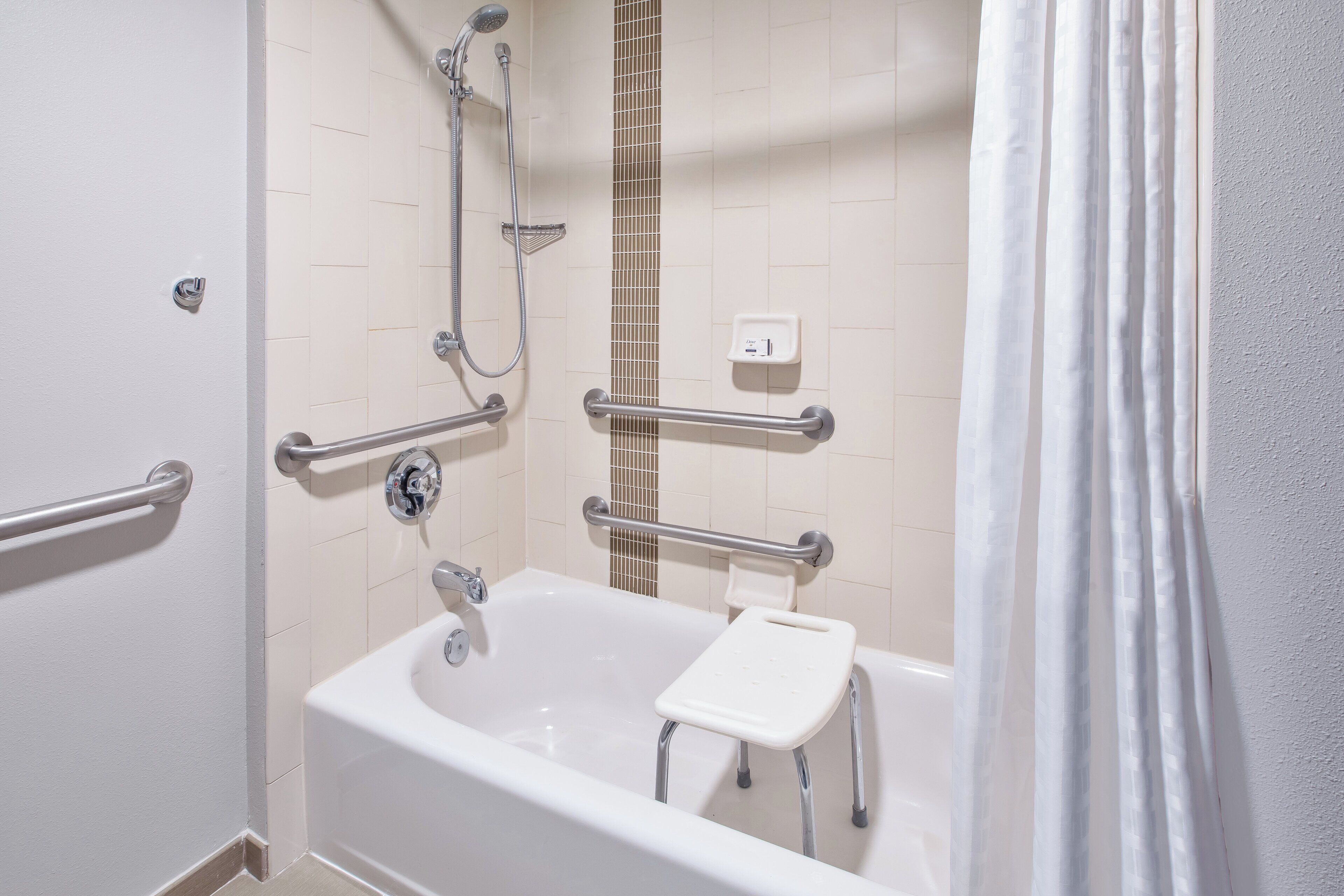 Een badkamer met een wit bad, grepen, een douchekop en een klein wit krukje.