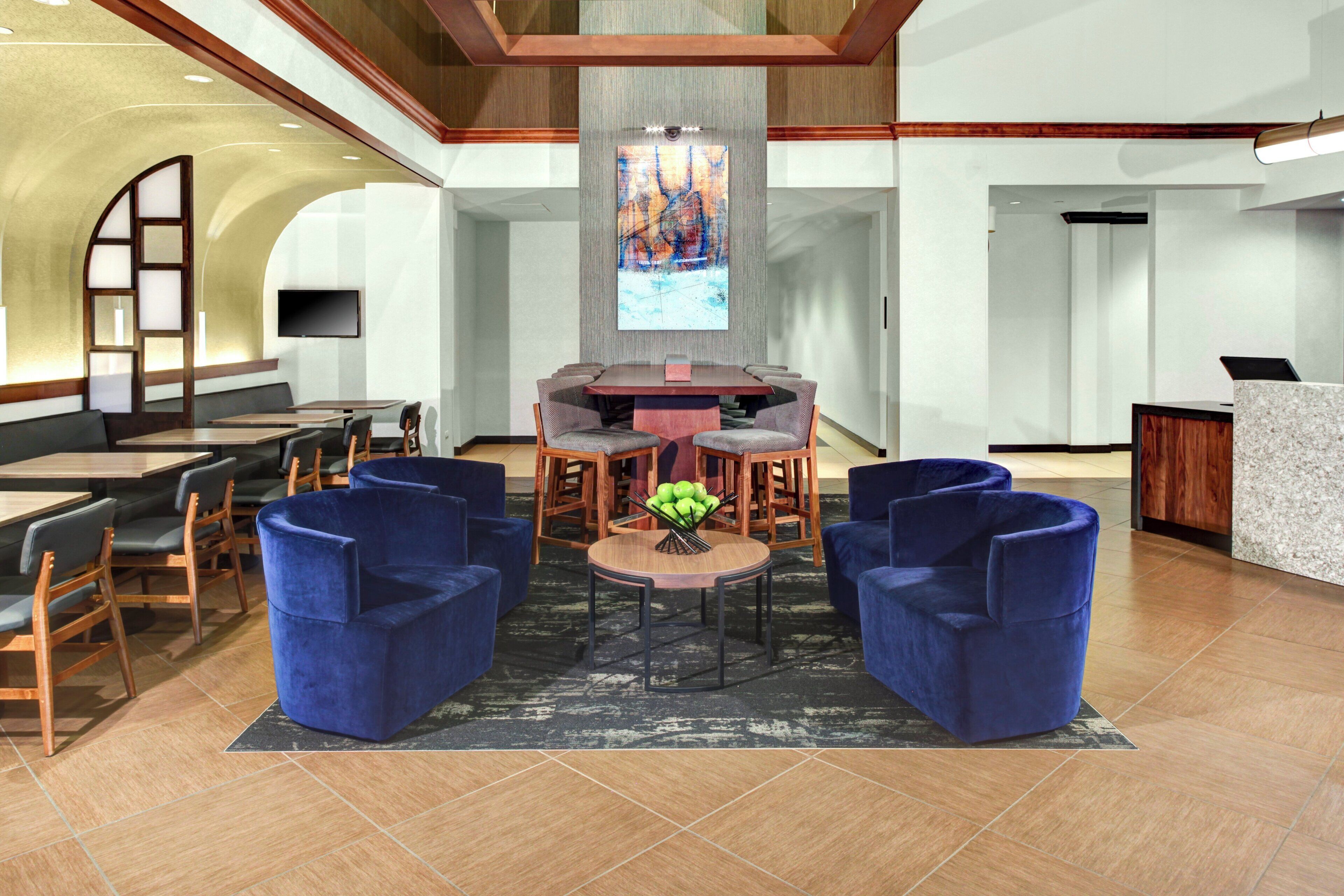 A lobby with a round table, blue chairs, a flat-screen TV, and a reception desk.