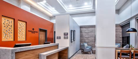 Ein Hotel-Empfangsbereich im modernen Stil mit einer Rezeption, einer Sitzecke mit Stühlen und einer Holzwand mit der Aufschrift 'CANDLEWOOD SUITES'.