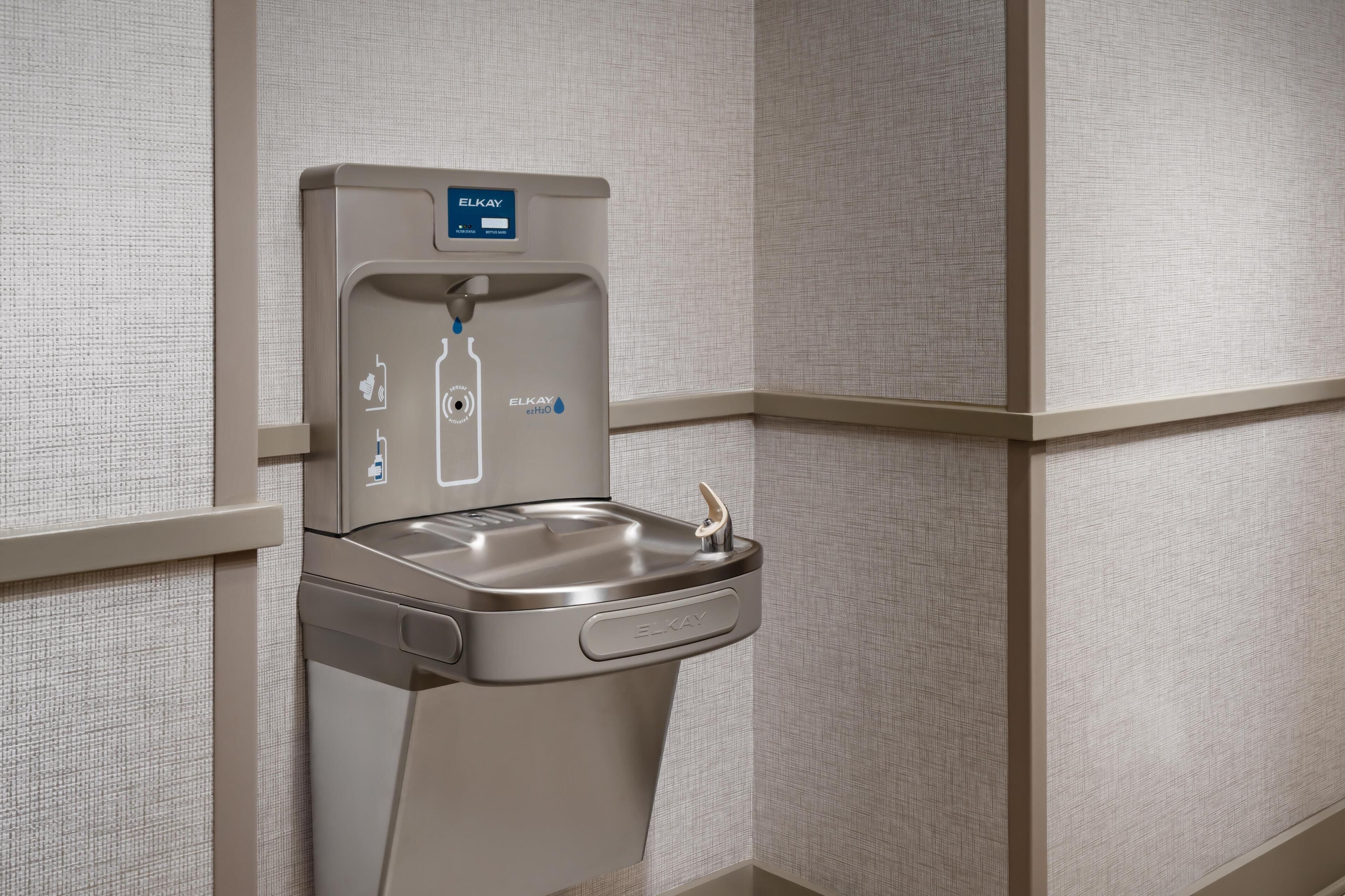 Een wandgemonteerd waterdispenser met een digitaal scherm, een kraan en een handdesinfectiepompen.