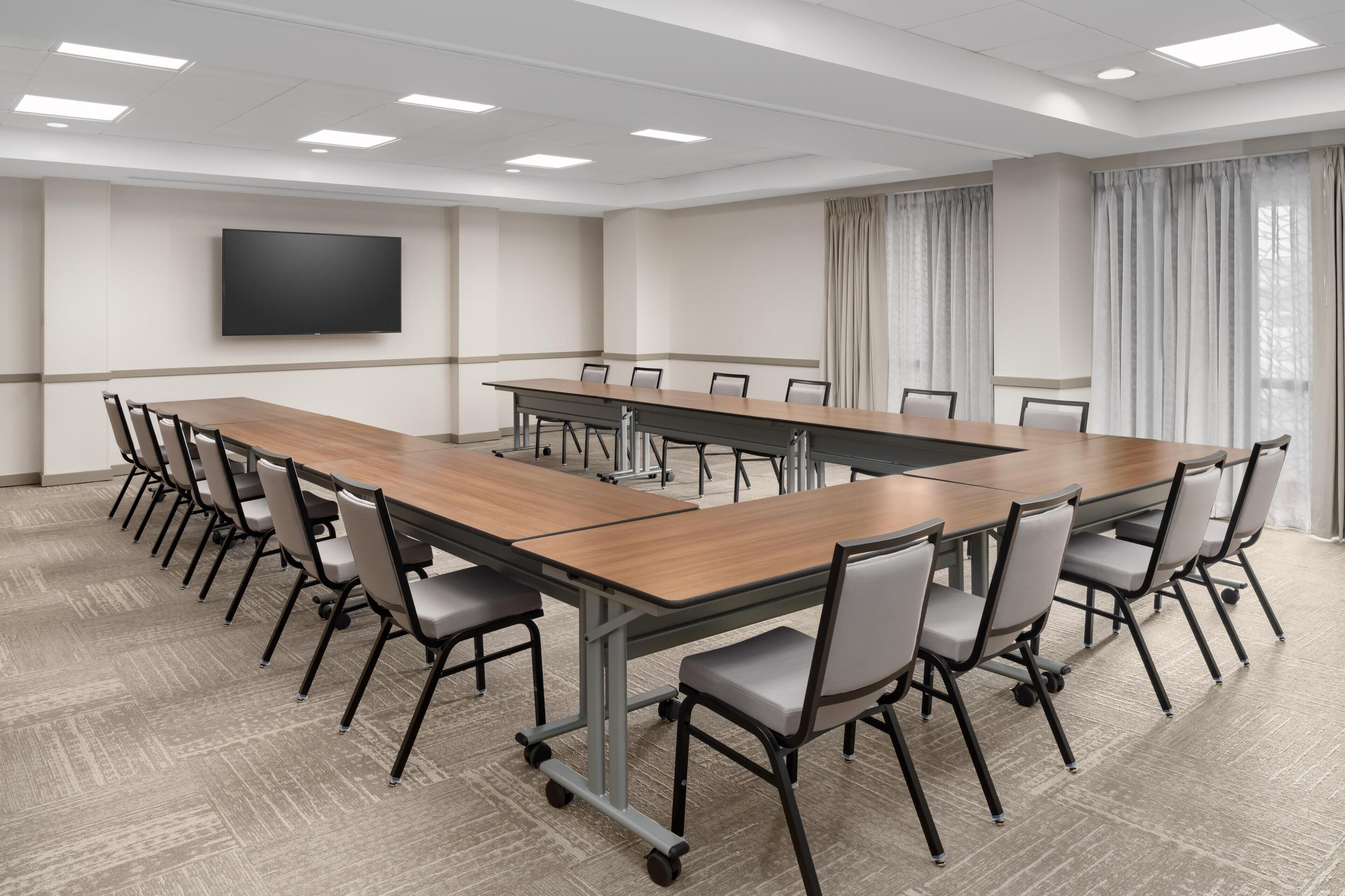 Un salón de conferencias con una larga mesa, sillas, un televisor de pantalla plana y cortinas.