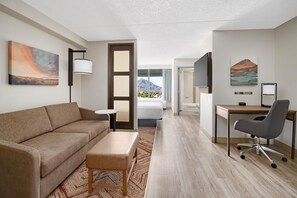 Ett modernt hotellrum med en soffa, ett skrivbord, en stol, en säng och ett stort fönster med utsikt över bergen.