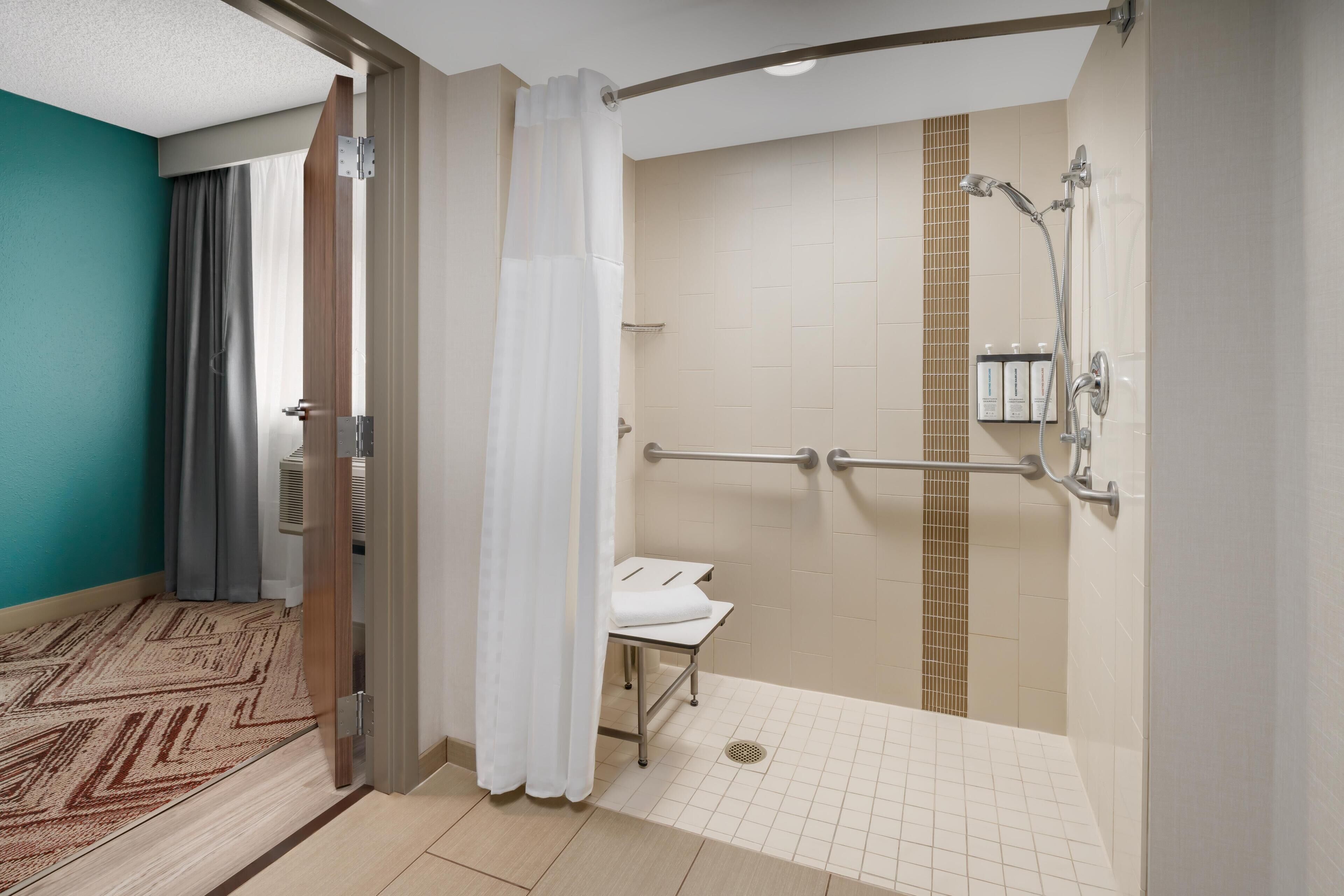 Un baño de hotel con ducha, un banco y una barandilla.