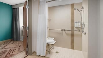 Un baño de hotel con ducha, un banco y una barandilla.