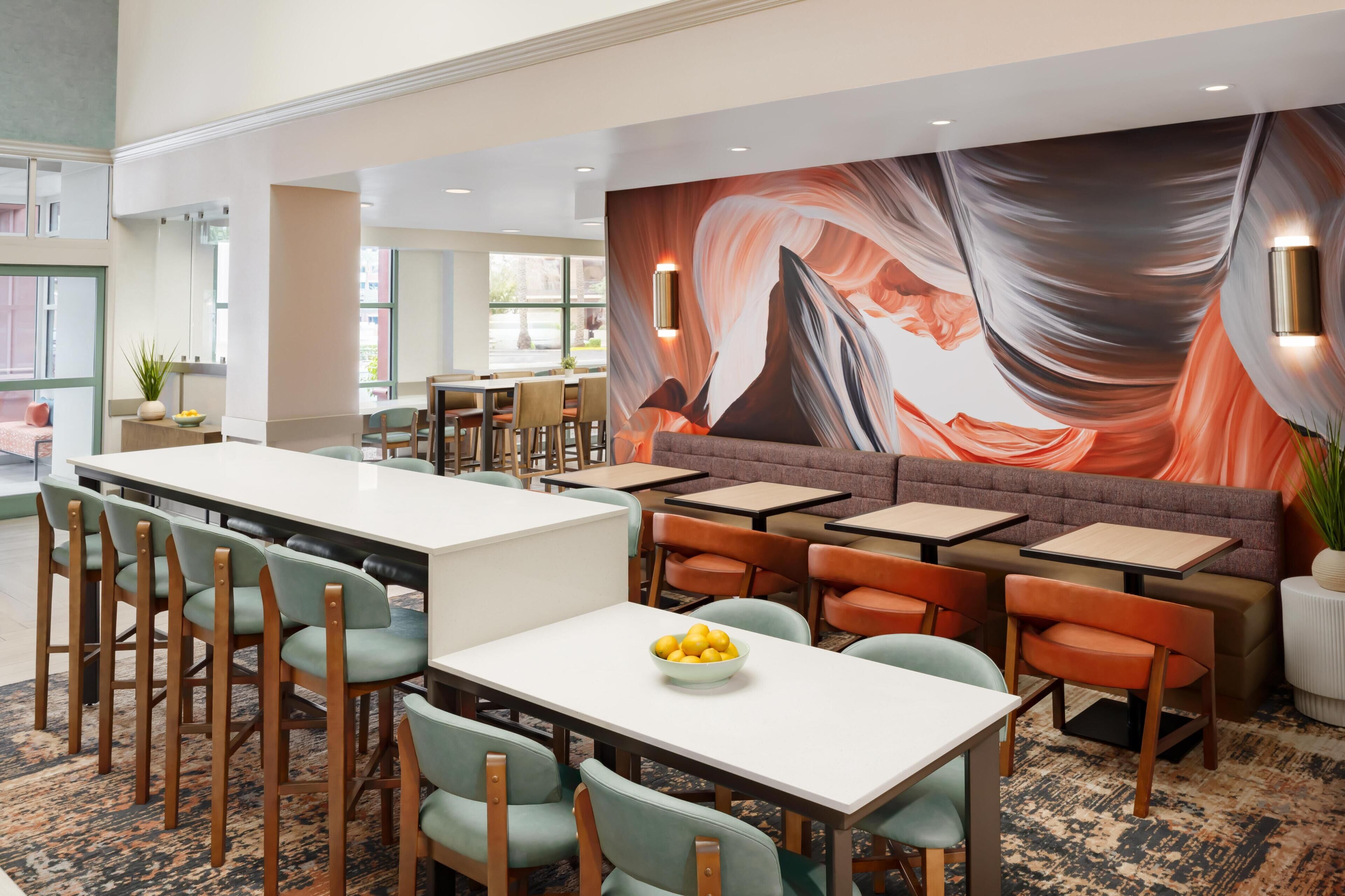En moderne restaurant med et langt fællesskabslangebord, separate spiseborde og et muralmaleri på væggen.