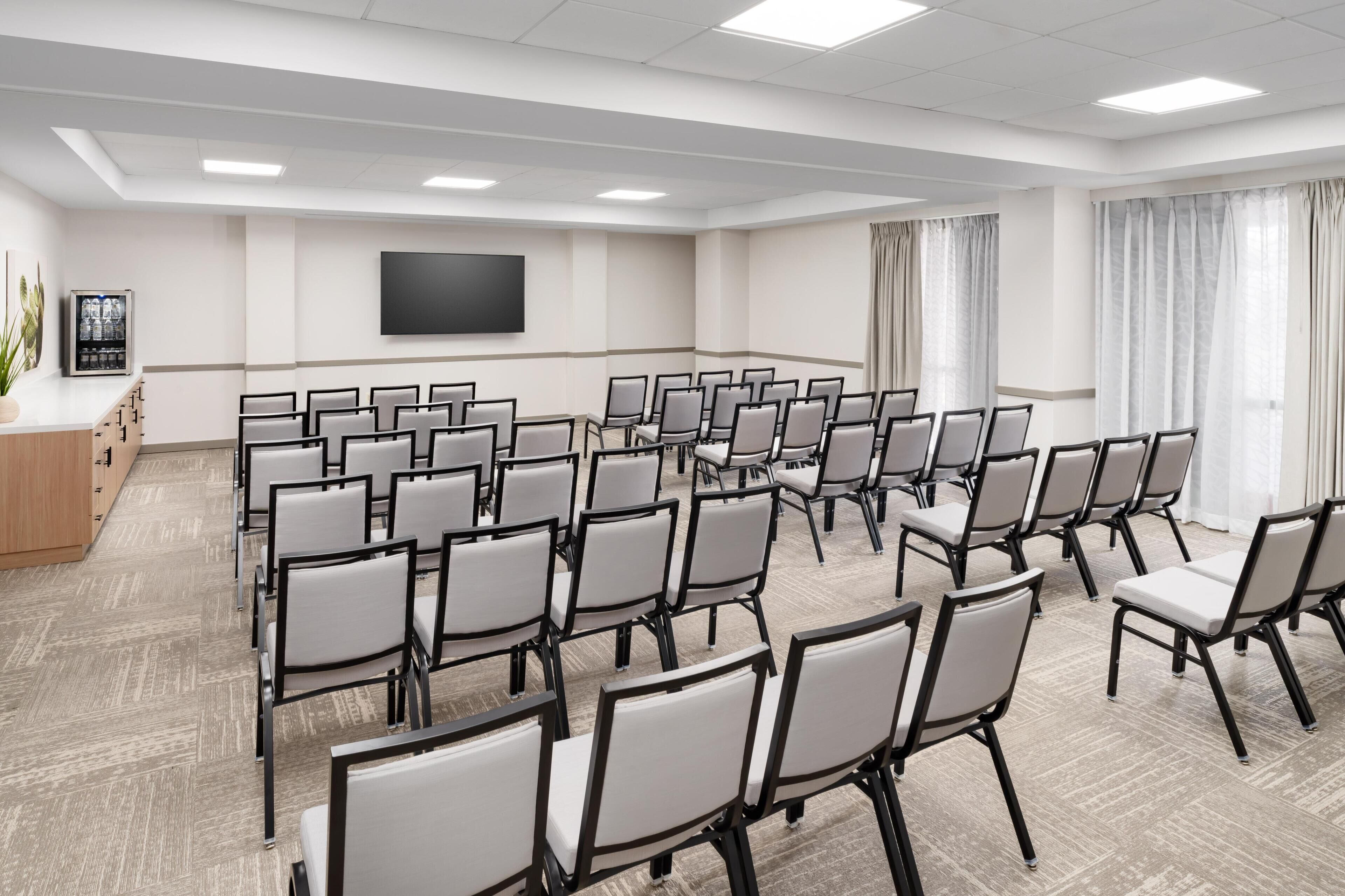 A conference room with rows of chairs, a flat-screen TV, and a plant.