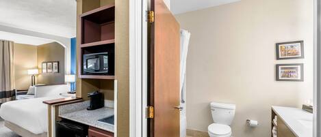 A hotel room with a bed, kitchenette, microwave, and a bathroom with a toilet and sink.