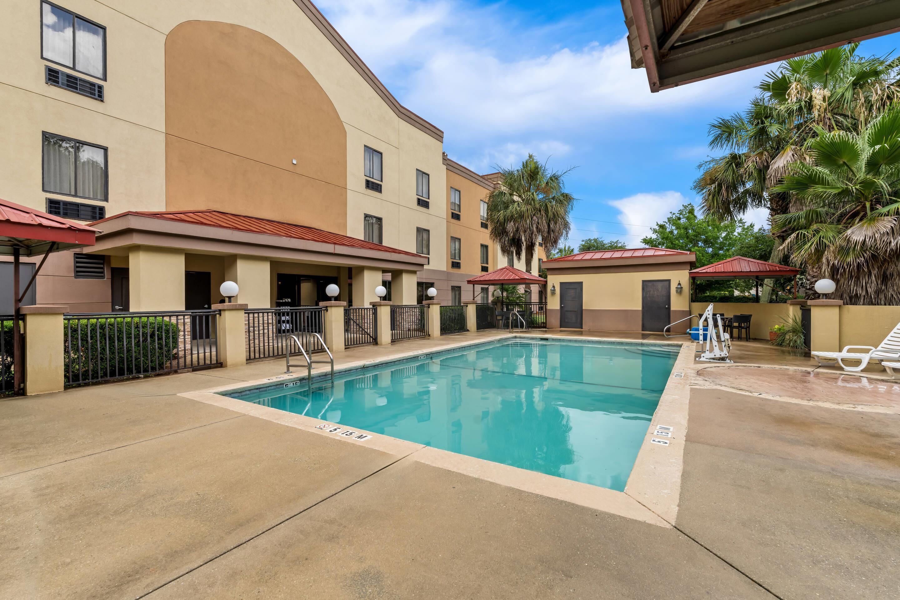 A hotel pool area with a clear blue pool, a covered seating area, and palm trees.