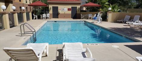 A swimming pool with lounge chairs, a covered seating area, and a building with a red roof.