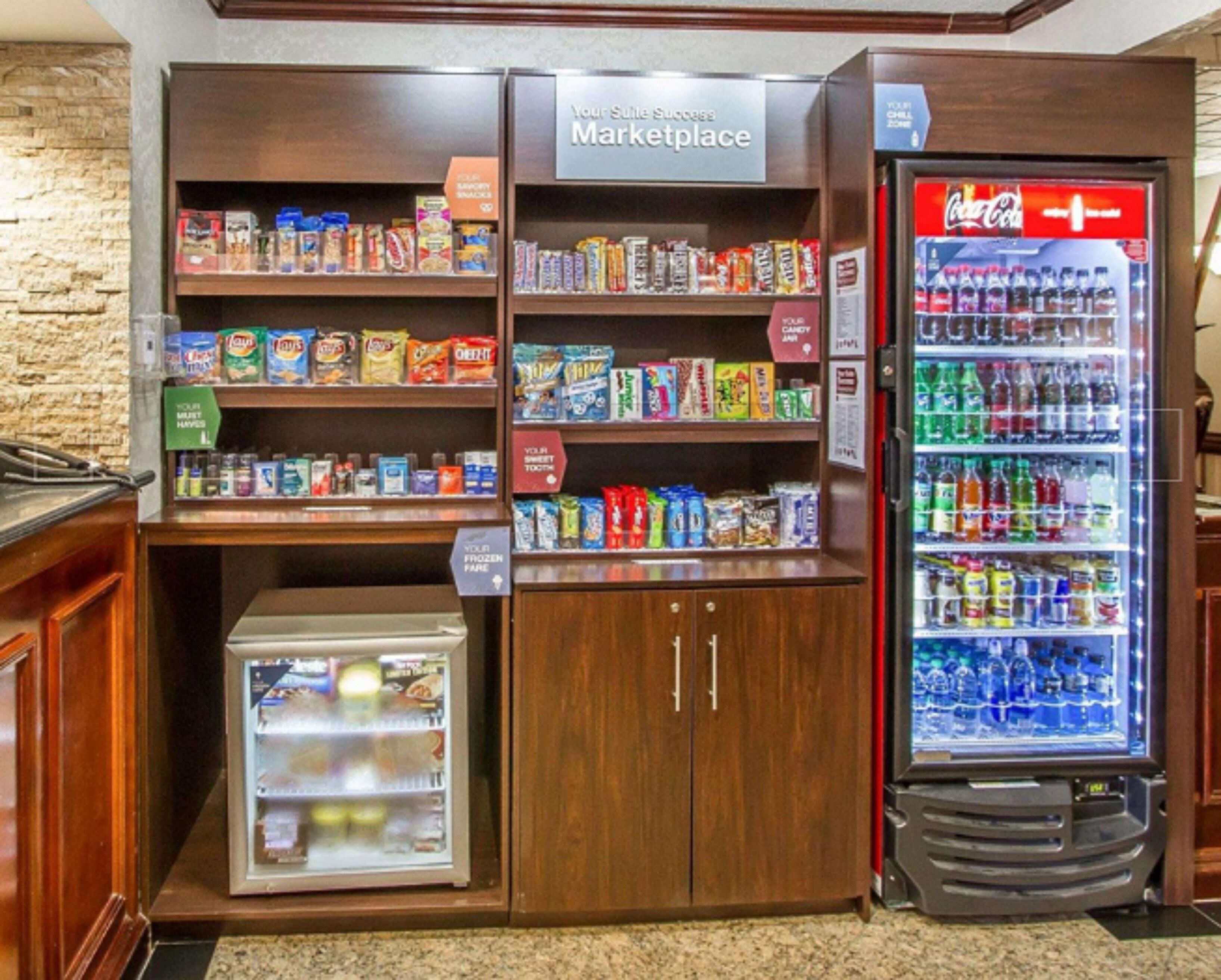 Eine Küchenzeile mit einer Mikrowelle, einem Kühlschrank und Regalen voller Snacks und Getränke.