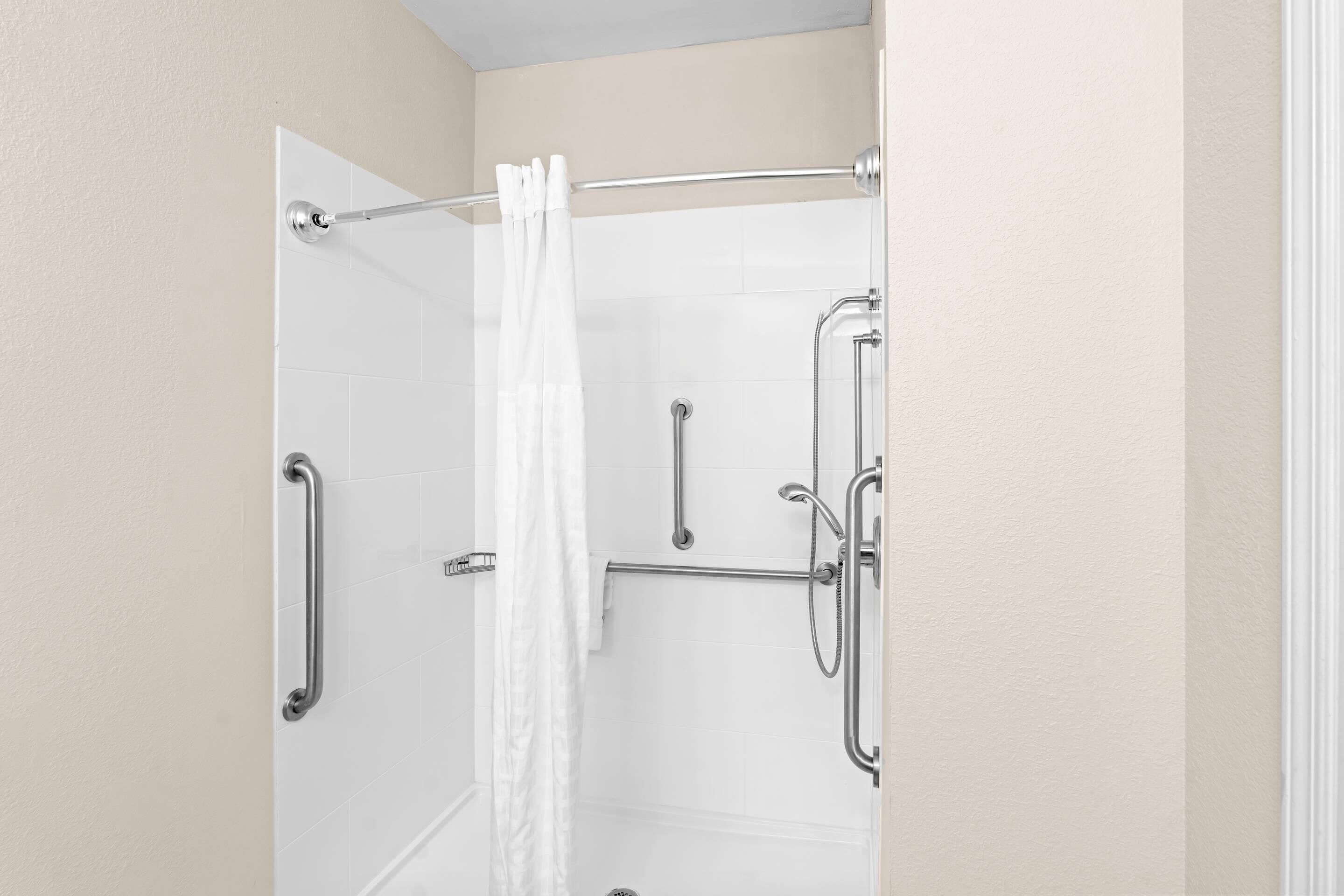 A shower area with a white curtain, a grab bar, and a handheld showerhead.