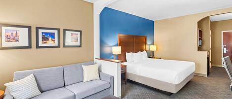 Habitación de hotel con cama, sofá, una mesita y un buró con lámparas. Se observan cuadros en la pared y una pared de acento azul.