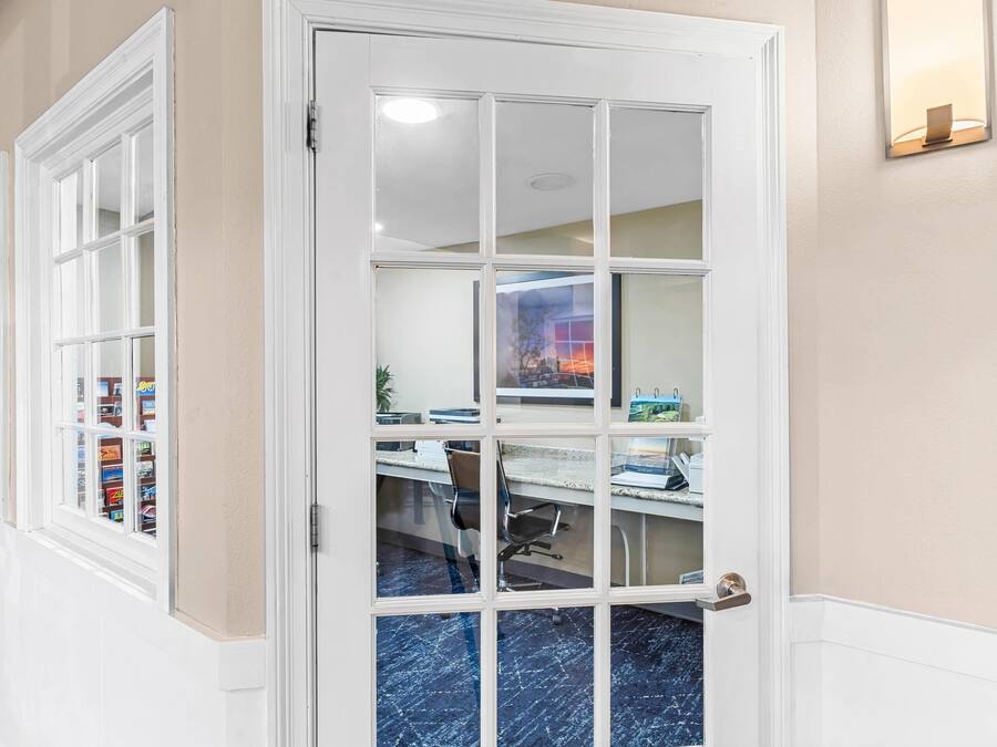 A hallway with a white door leading to a room with a desk, chair, and shelves with books.