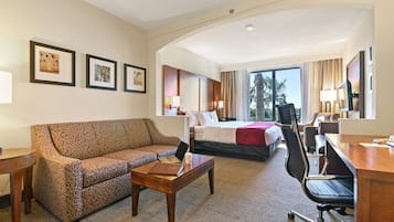 Habitación de hotel con sofá, escritorio, silla, cama, lámpara de escritorio y cuadros en la pared.