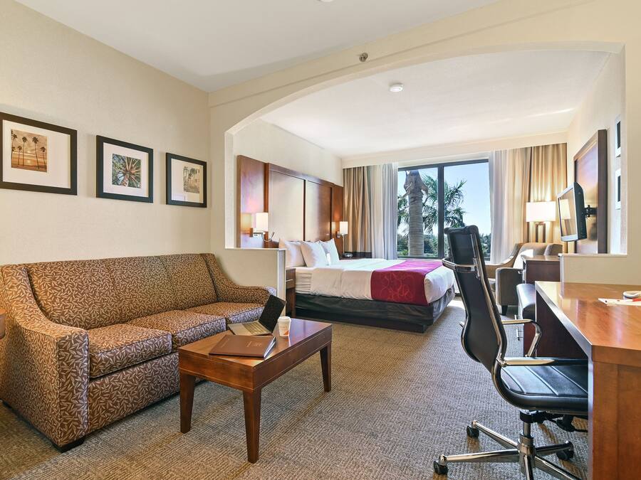 Habitación de hotel con sofá, escritorio, silla, cama, lámpara de escritorio y cuadros en la pared.