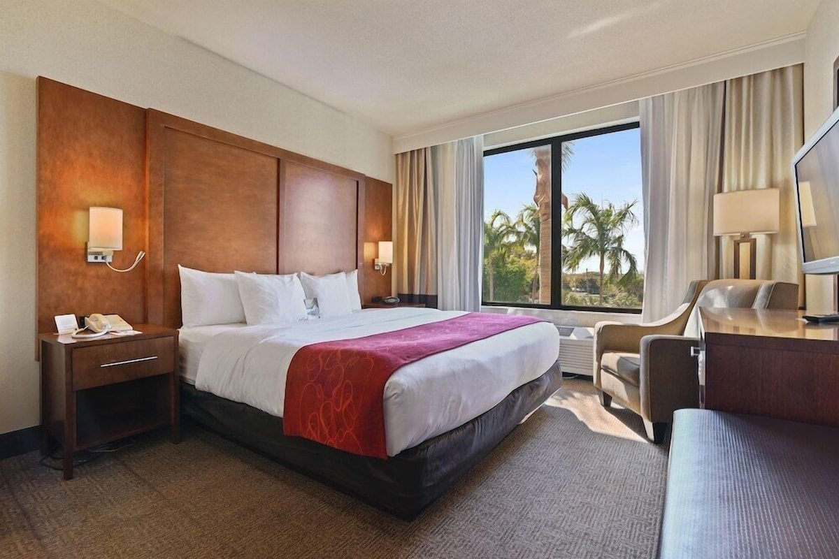A hotel room with a large bed, a desk, a chair, and a TV.