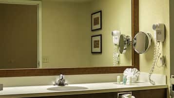Un baño de hotel con lavamanos, espejo, secador de pelo y toallero.