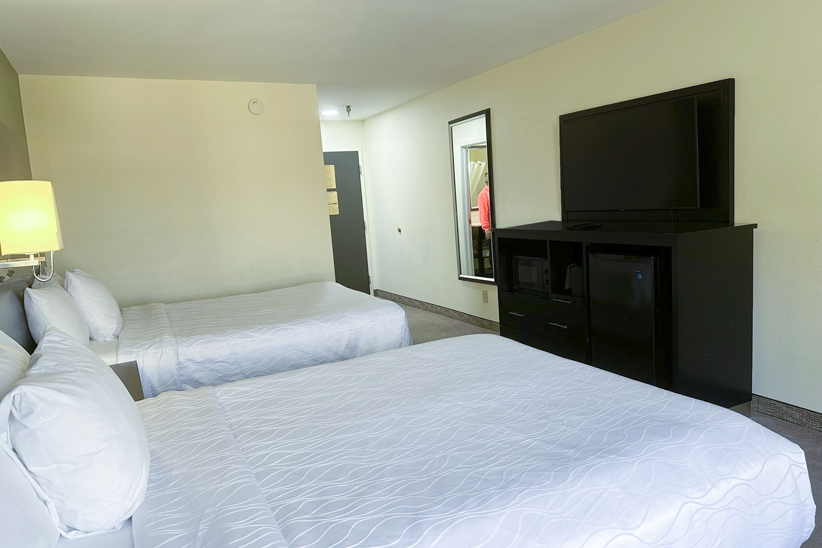 A hotel room with two beds, a TV, a mirror, and a dresser.