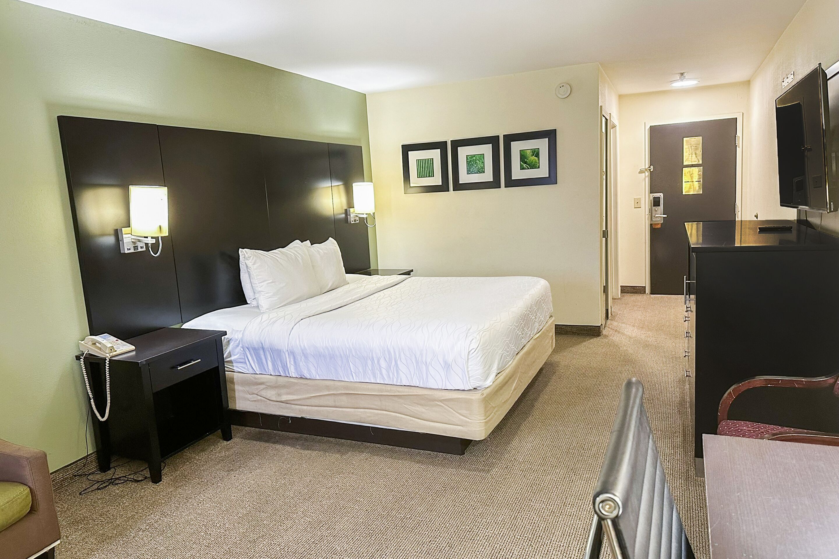 A hotel room with a bed, bedside table with a phone, wall-mounted lights, and a TV.