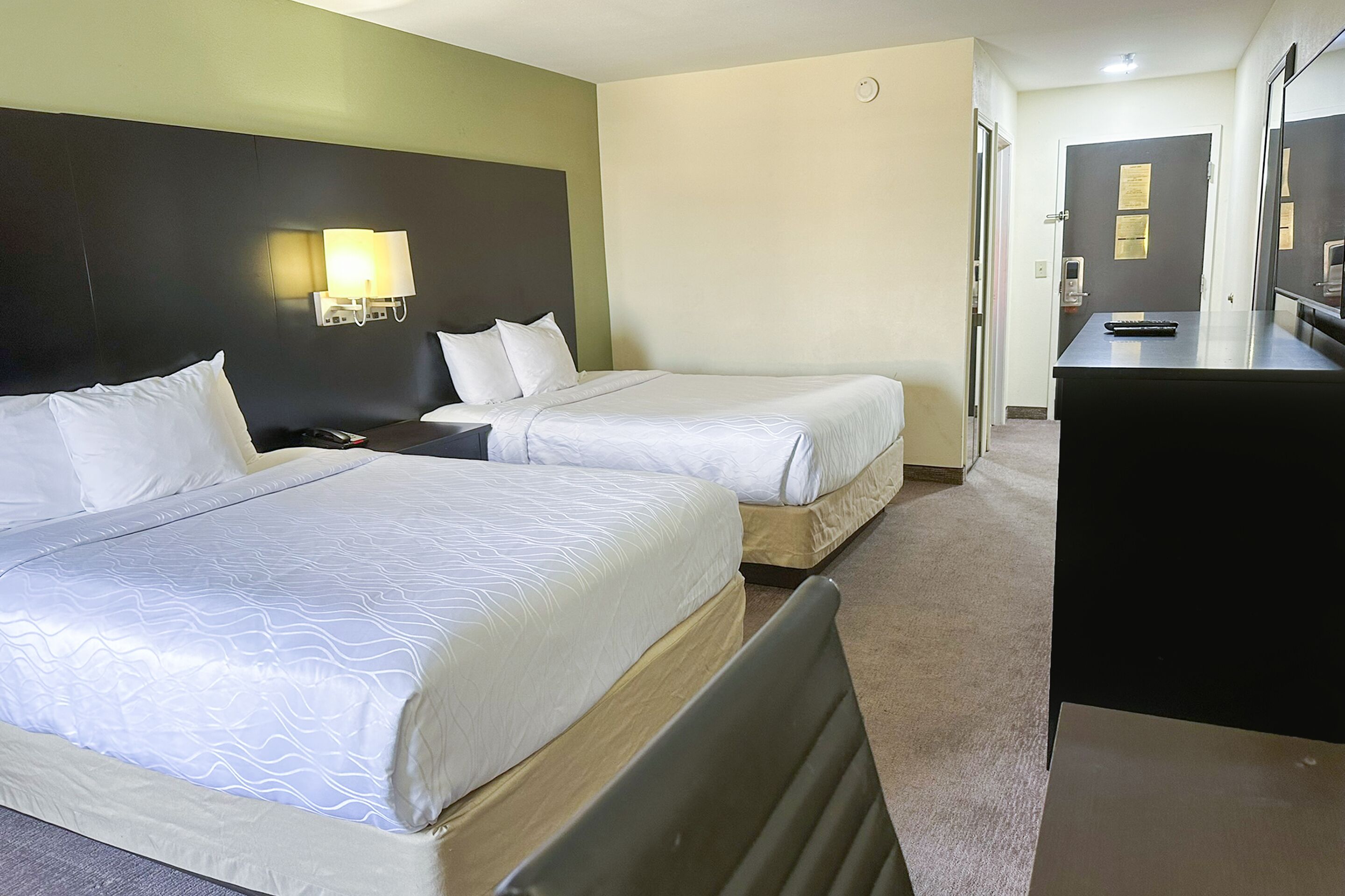 A hotel room with two beds, a desk, and a mirror.