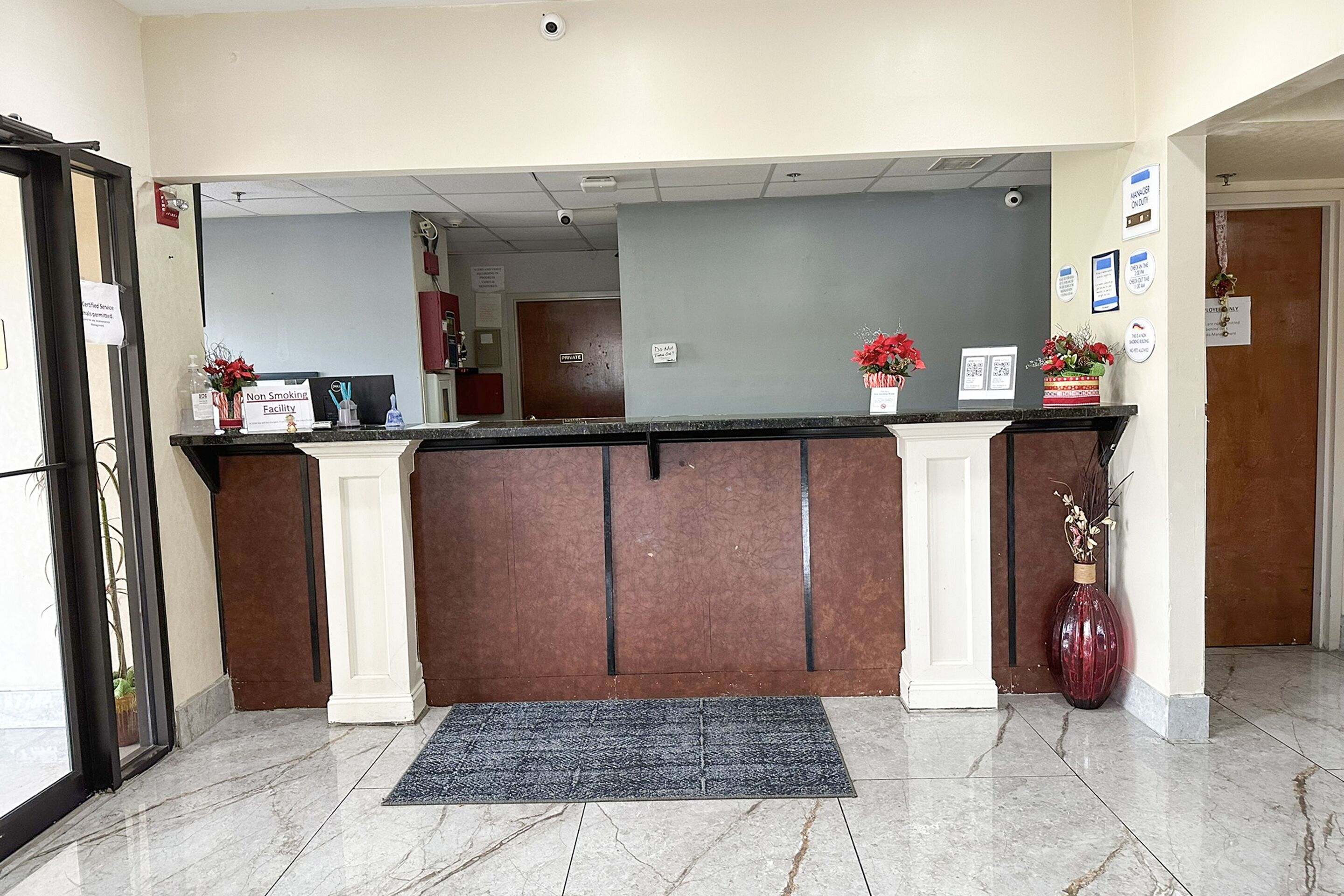 A reception area with a marble floor, a black reception desk, and a red vase with flowers.