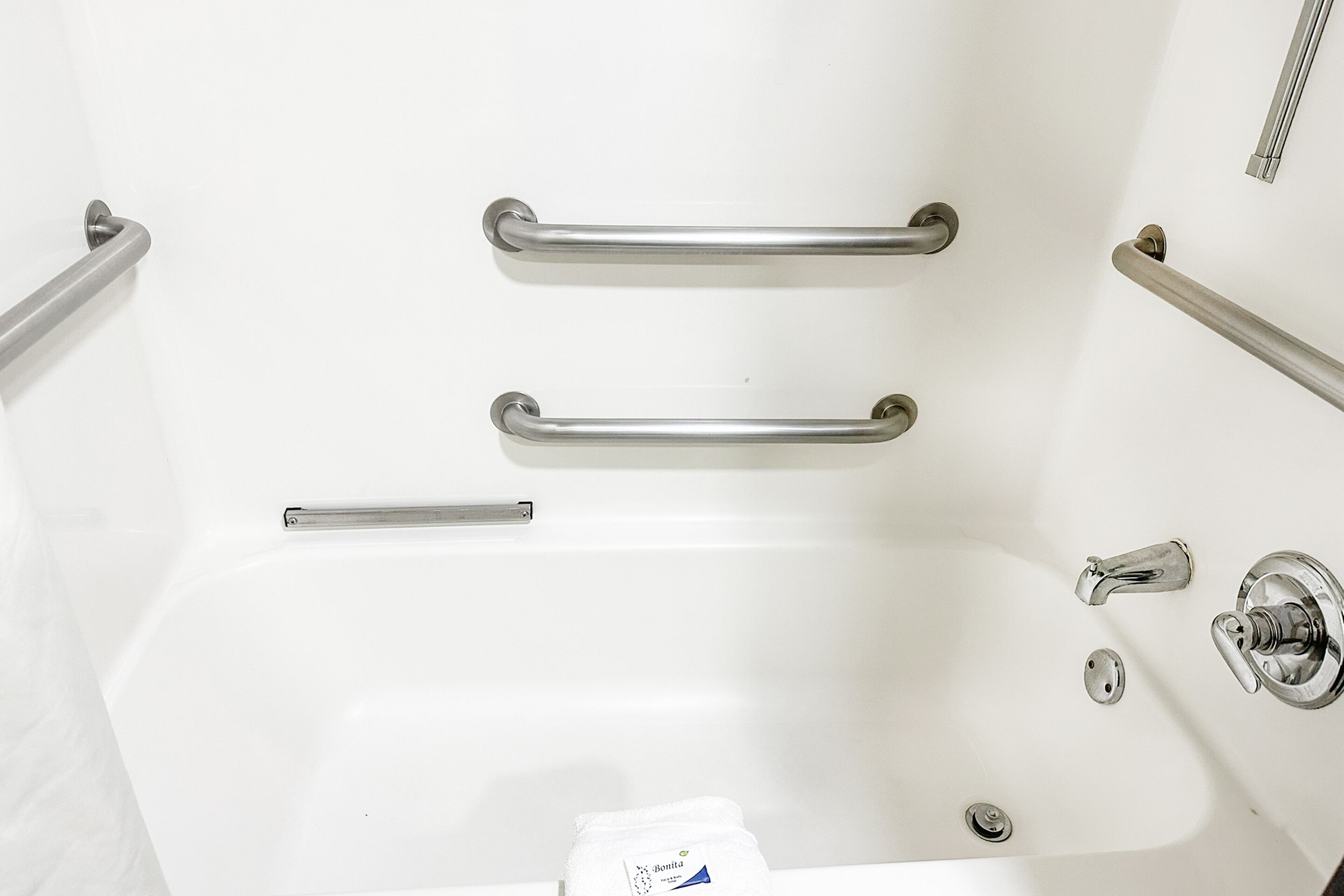A white bathtub with two grab bars and a faucet.