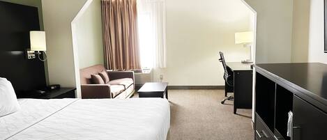 A hotel room with a large bed, a desk, a chair, a sofa, a TV, and a wardrobe.