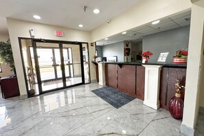 A reception area with a marble floor, a reception desk, a plant, and an exit sign.