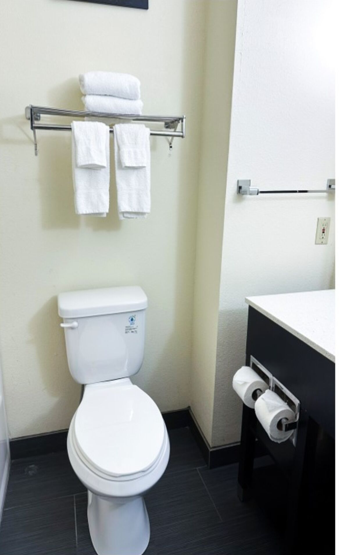 Une salle de bain moderne avec des toilettes blanches, un porte-serviettes avec deux serviettes et un support à papier toilette.