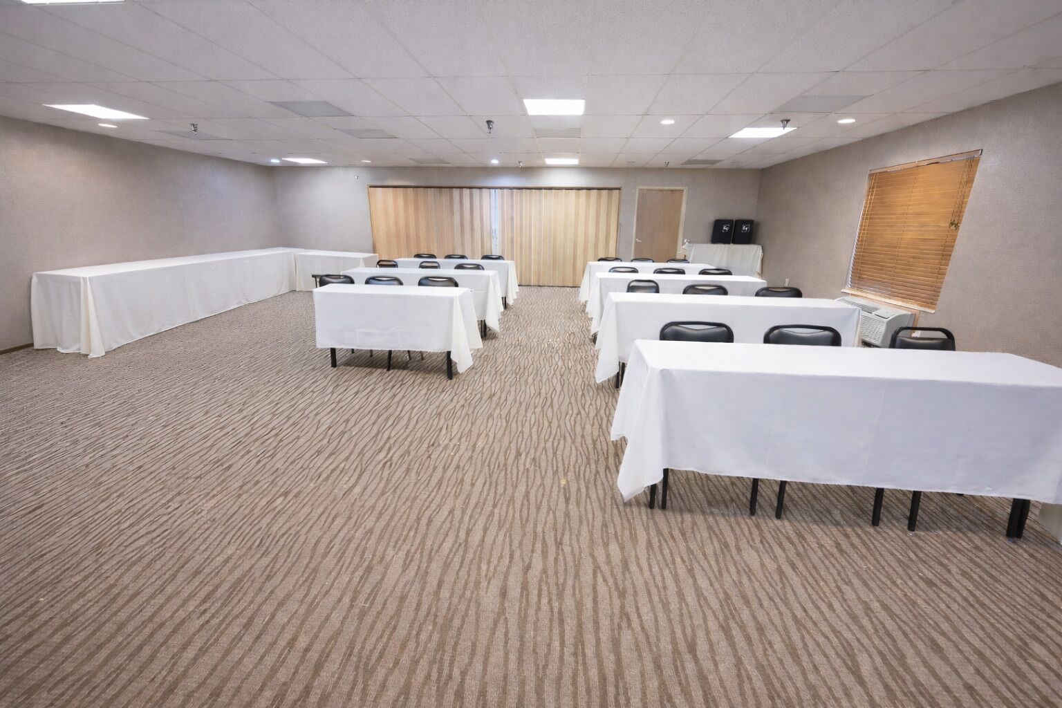 A conference room with multiple tables and chairs, carpeted floor, and a wooden door.